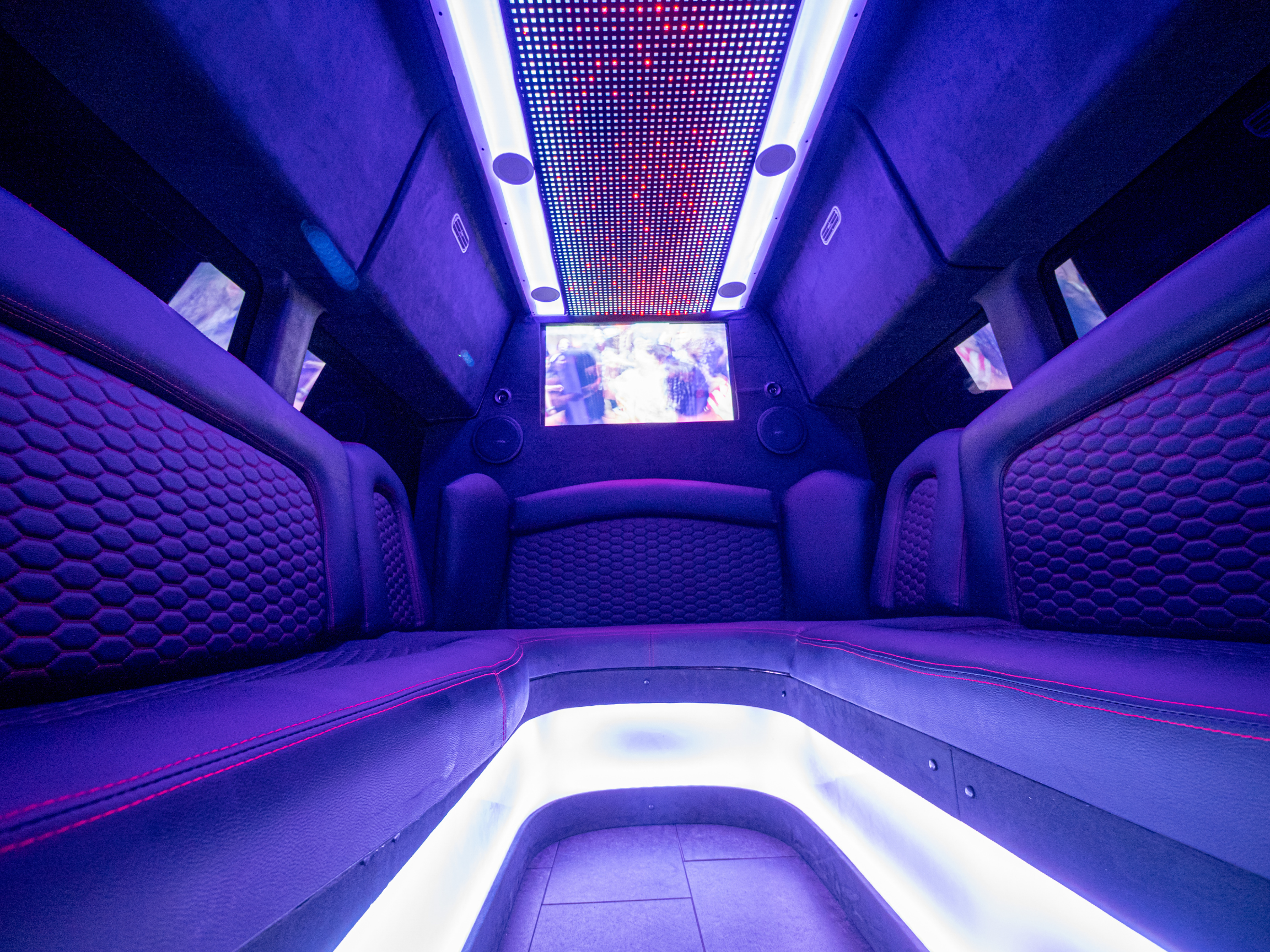 Interior of Van Limo party bus in Puerto Rico with purple ambient lighting, leather seats, and two TV screens