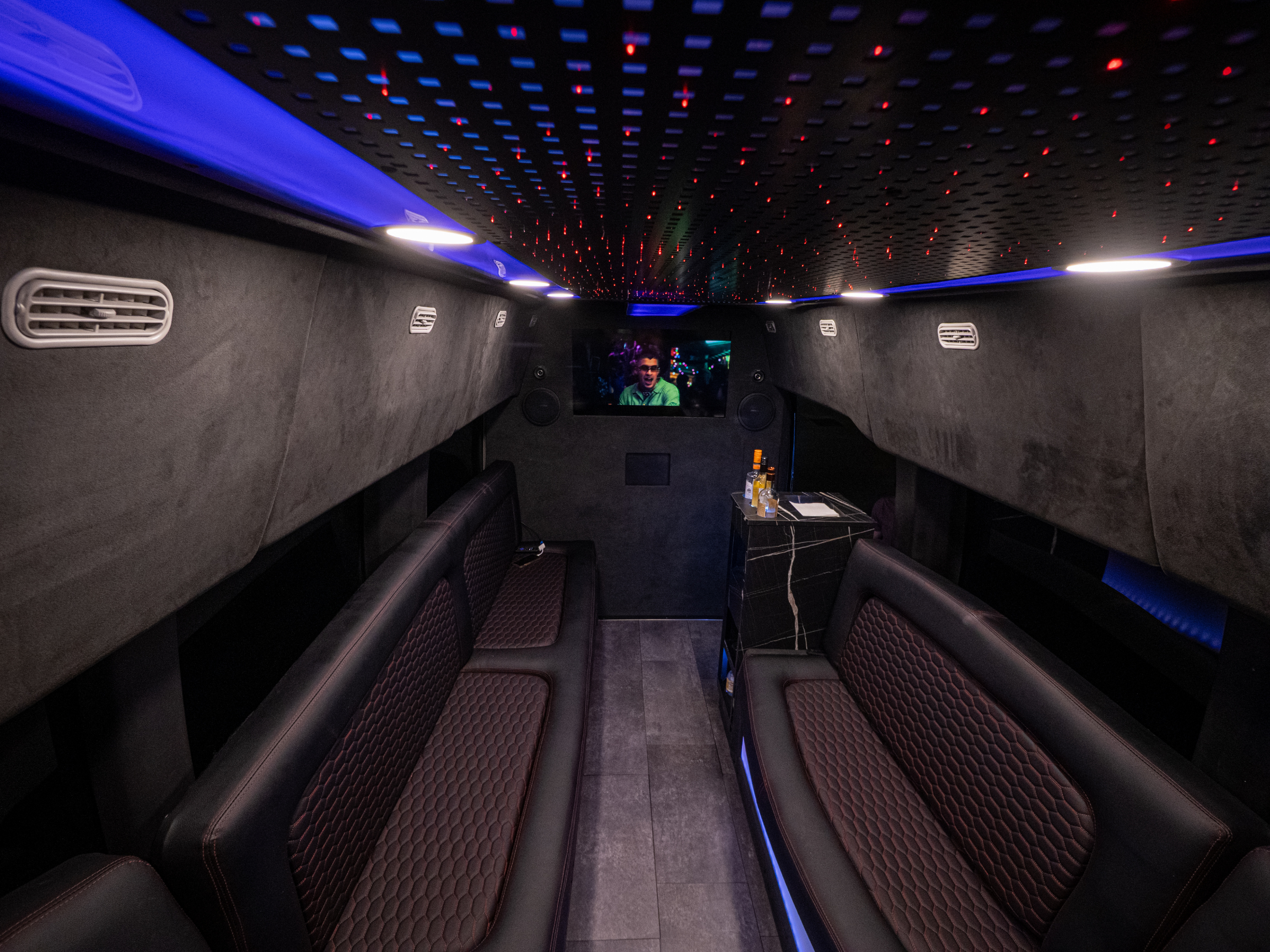 Van Limo party bus interior in Puerto Rico with LED ceiling, leather seating, minibar, and TV showing concert
