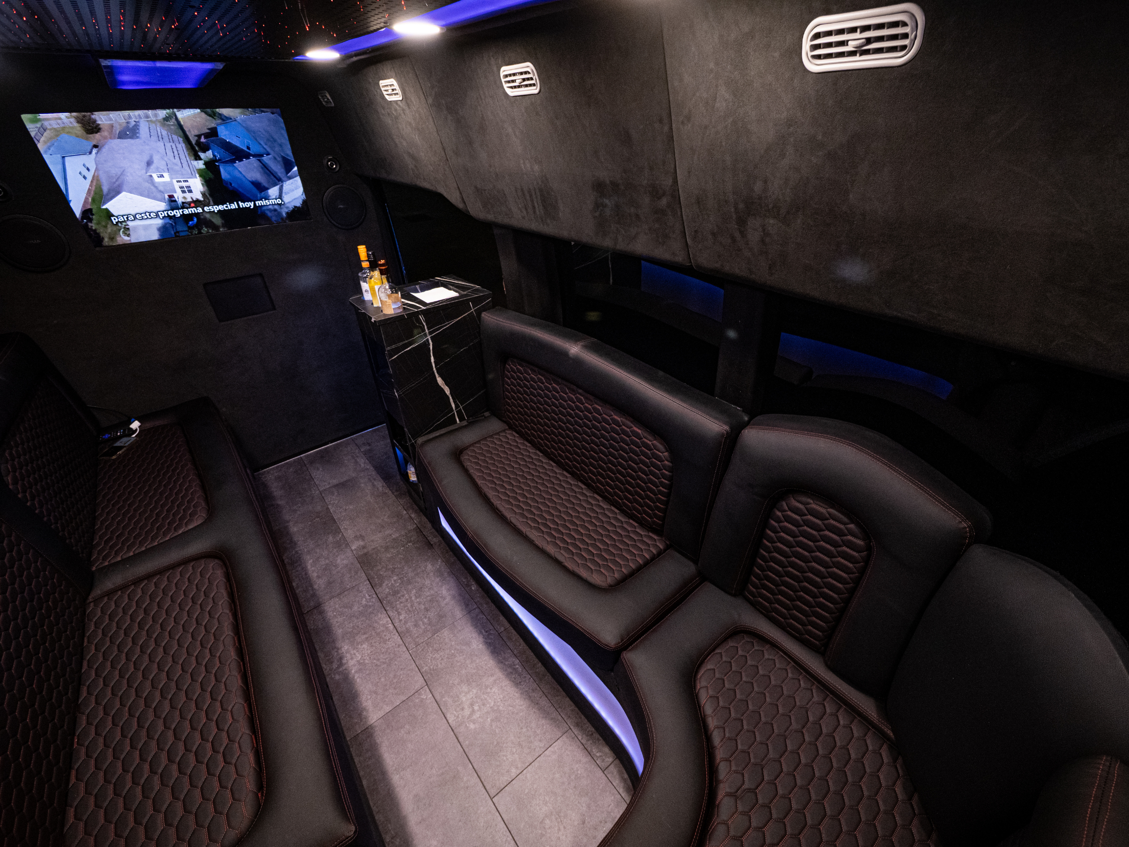 Van Limo party bus interior in Puerto Rico featuring curved leather seating, minibar and TV screen with Spanish program