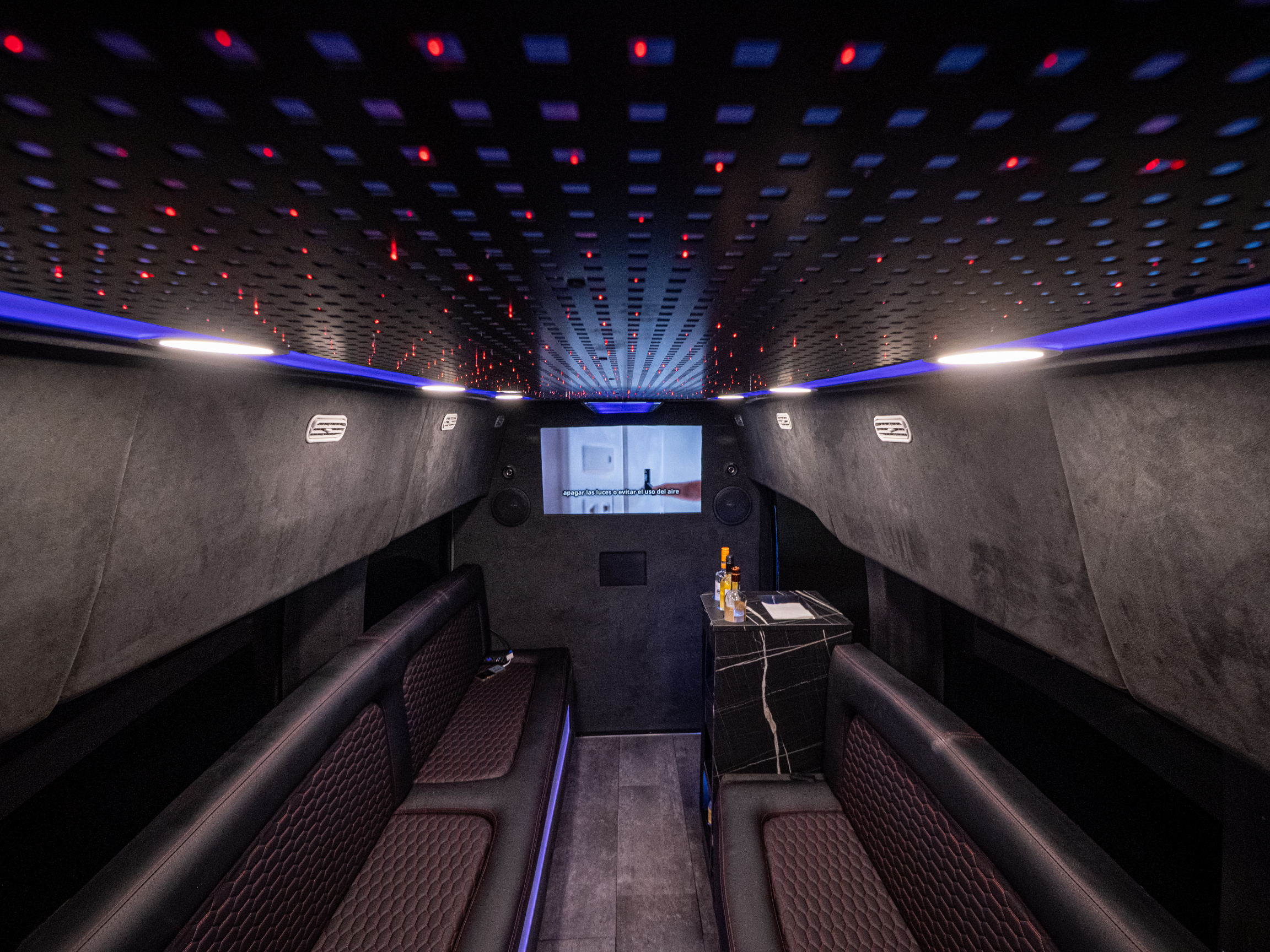 Wide-angle shot of Van Limo interior in Puerto Rico with LED ceiling, leather seats, and minibar