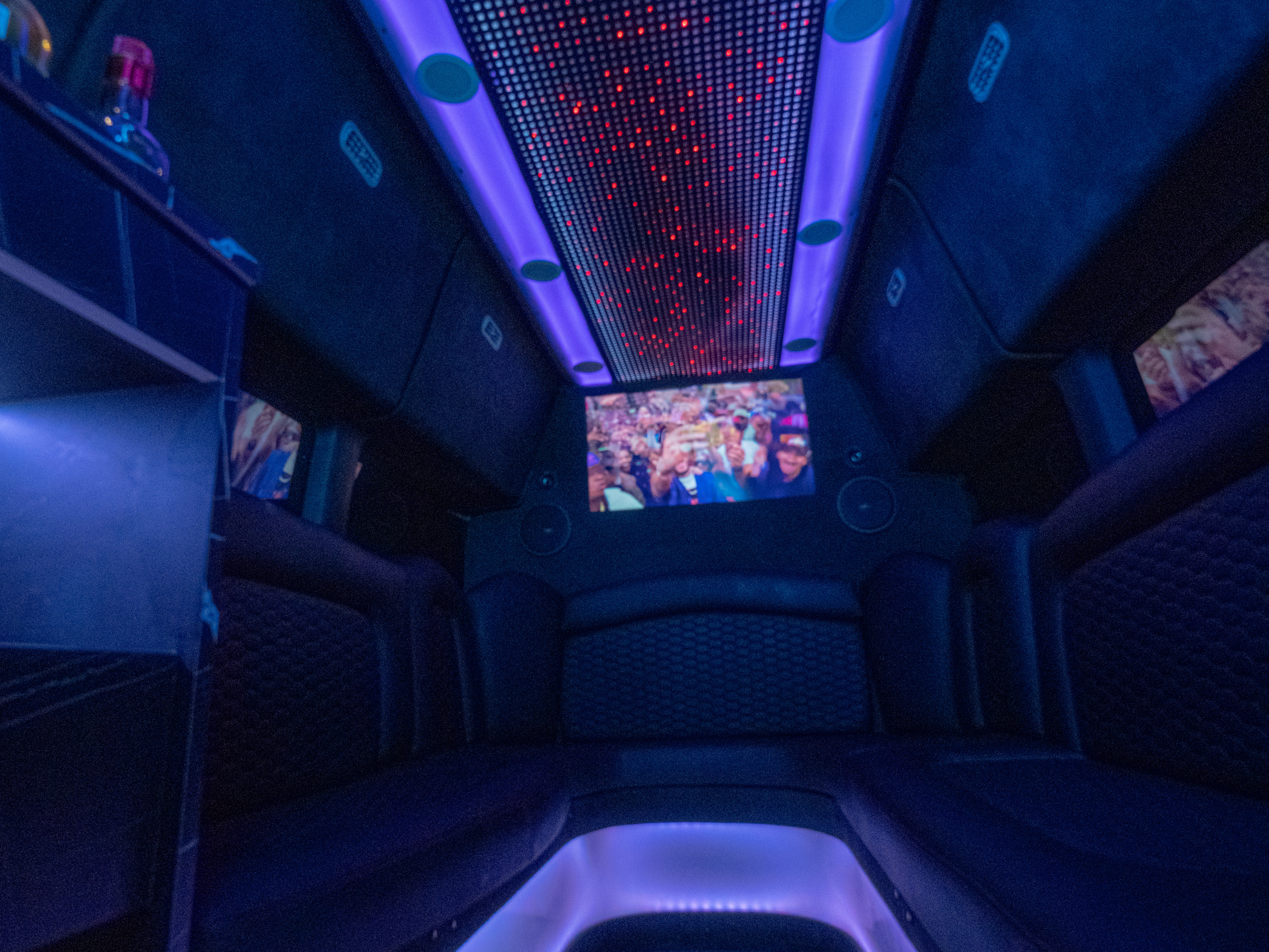 Van Limo party bus interior at night with LED ceiling, leather seating, and onboard entertainment screen in Puerto Rico